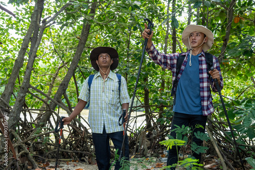 Two male friends with backpacks on vacation hiking through countryside together. Man tourists with backpacks and hiking equipment are walking in the forest. People on mountain hike with trekking poles