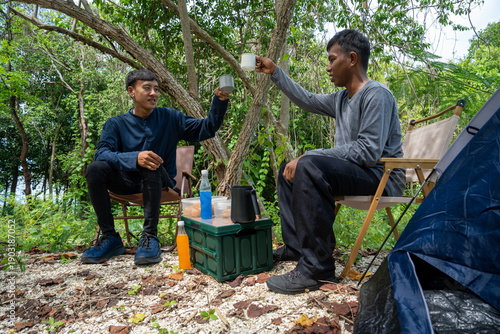 Two man tourists backpacking and relaxing on picnic in forest with camping equipment. Man pitching tent on camping trip. Vacation concept on a sunny summer day.