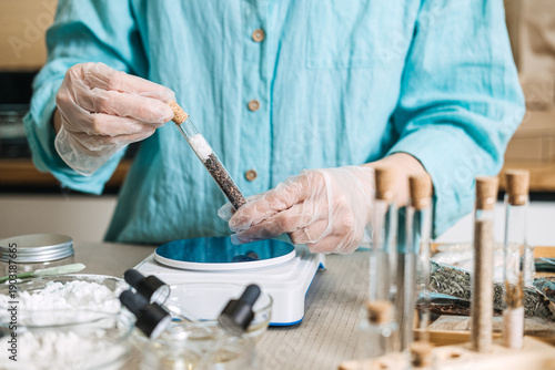 Fotografija Gloved hands hold glass test tube filled with salt and botanical layers near digital scale