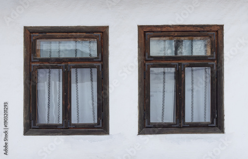 Two vintage wooden windows with white curtains on a rustic white wall