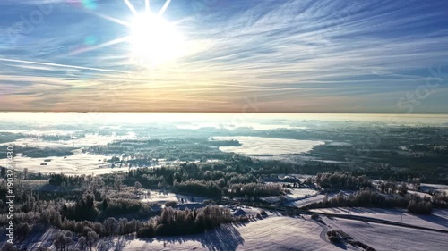 Bright winter aerial with low sparkling daze sun above snowy landscape and layered clouds, forest backdrop background