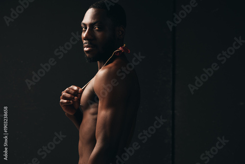 African man with dark skin and muscular body posing shirtless in creative conceptual visual style with serious expression on black background for artistic portrait photography.