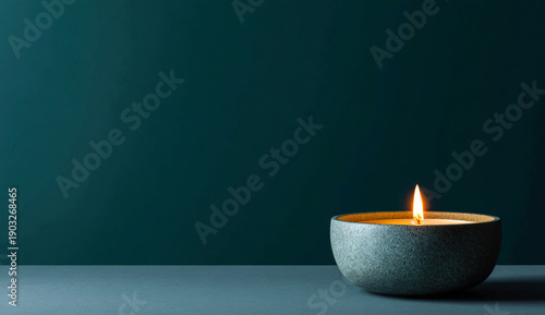 Minimalist teal background with a single lit candle in a smooth gray stone holder, creating a calm and serene atmosphere