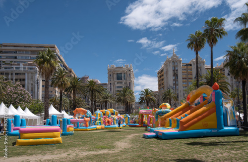 Wallpaper Mural Inflatable slides, bounce castles, and obstacle courses set animated movie on a grassy urban park with palm trees and tall buildings in the background during daytime outdoor event Torontodigital.ca