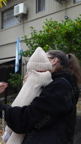 mother holding and kissing her newborn baby outdoors in a residential neighborhood. 
