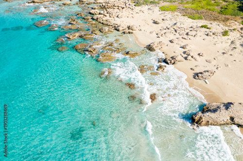 Photos Aerial view of clear turquoise water washing over scattered rocks and pale sand at Falasarna Beach, Crete