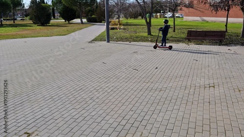 Young boy with helmet riding an electric scooter in a city park