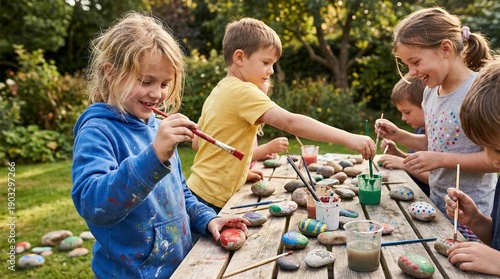 Children painting rocks together outdoors in sunny garden setting  