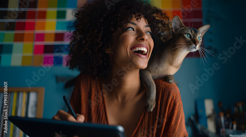 Young black woman laughing at desk with cat beside her and colorful swatch wall