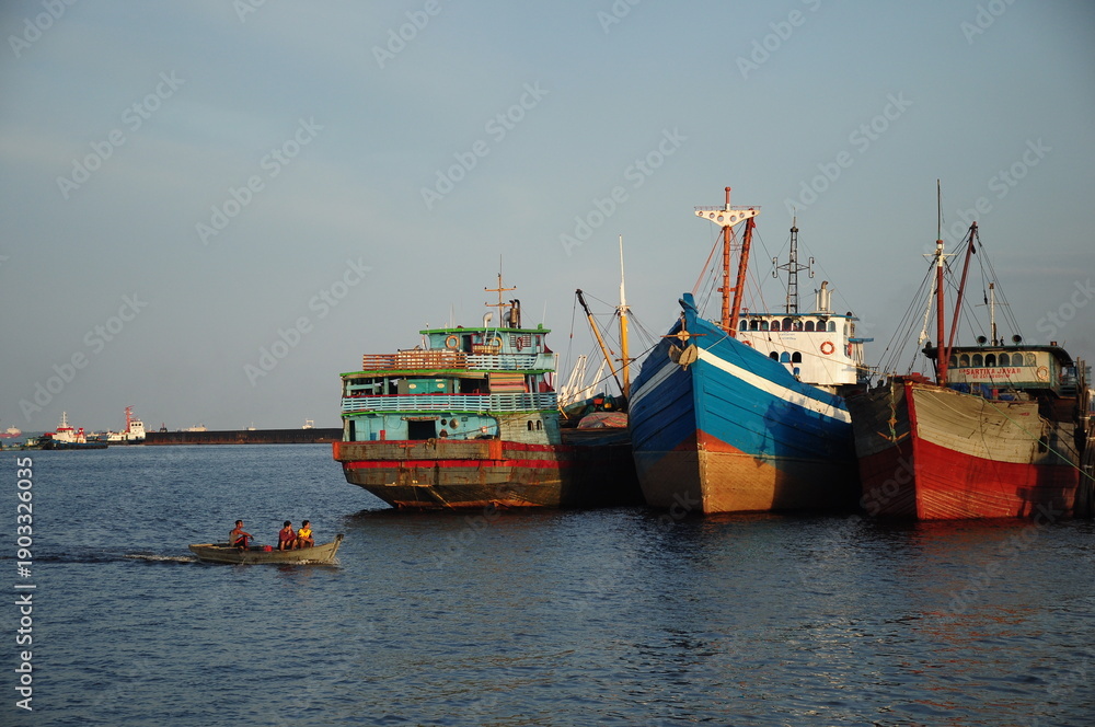 Obraz premium A row of colorful traditional fishing boats moored at the harbor in the afternoon with small boats passing through the calm waters.