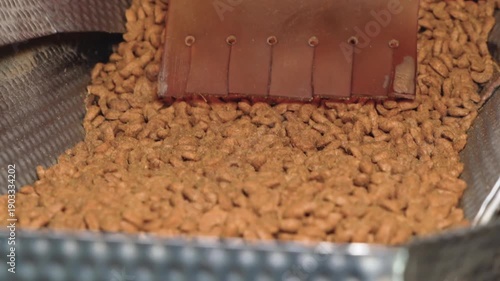 Close up of dry pet food kibble dropping from a manufacturing machine hopper during food production process