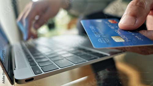 Close-up of hands holding a credit card near a laptop keyboard, emphasizing online shopping and contactless payment. The setting suggests a secure, modern transaction, highlighting digital finance.