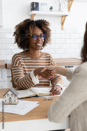 handshake between two people, conclusion of contract for sale of real estate. architectural and design project contract. buying or renting an apartment. miniature model of house stands on table.