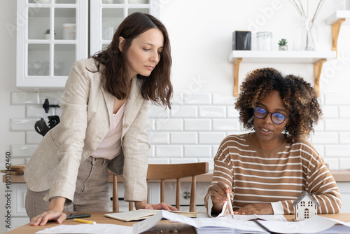 business person sitting at table, negotiating. two women are going through papers, discussing project. interior design, architectural bureau. diverse people, African American business woman realtor.
