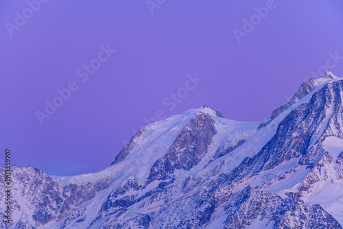 Snow-covered slopes and icy ridges of Mont Blanc du Tacul stand out beneath a striking violet twilight sky, creating a serene and dramatic alpine scene.