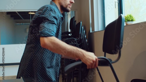 Man arranging chairs in office space during midday preparations for a meeting or event