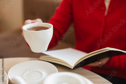 Close-up of a woman in a red cardigan organizing her schedule in a paper planner over tea.