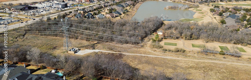 Panorama aerial view transmission corridor east of Lantana Trail spans wooded areas between residential streets, lakeside golf zone. Reflective water, winter trees, patterned roofs in Lantana, TX