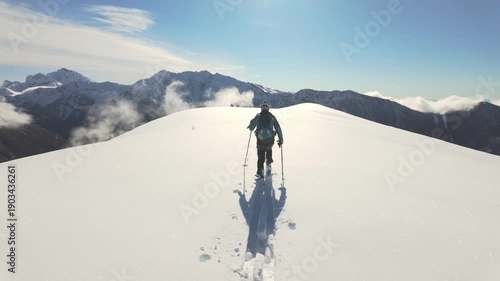 Ski mountaineer ascending snowy alpine ridge in winter mountains