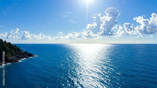 Aerial view shows the turquoise ocean meeting the y coastline under a bright blue sky with f clouds.