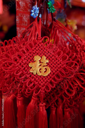 A traditional red Chinese knot decoration featuring an intricate woven pattern, long tassels, and a central gold character for 
