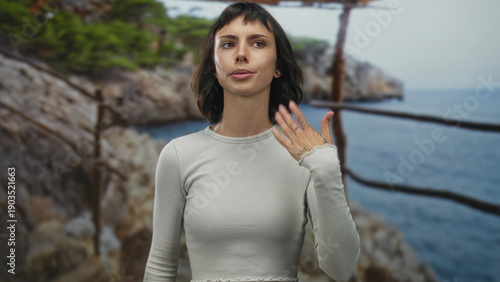 Canvas Print Young hispanic woman fans face with hands beside a rugged rocky coast railing in forest; relief from heat