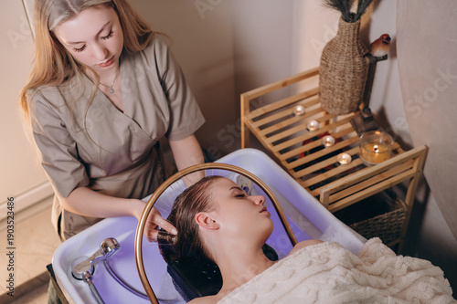 Young woman receiving a head massage during a Japanese head spa treatment with water flowing from a special hair washing tool.