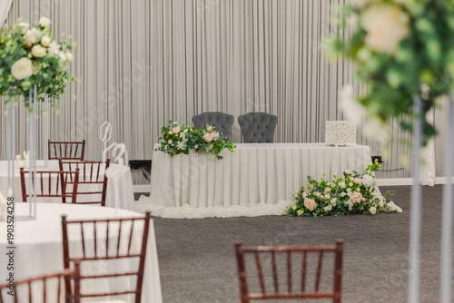 Decorated interior for festive event. Fancy table set for dinner with white flower composition in restaurant, luxury interior background. Wedding elegant banquet decoration arranged by catering