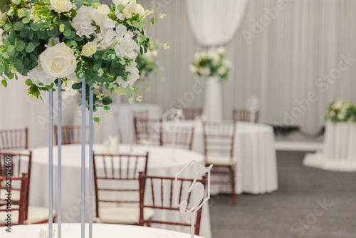 Decorated interior for festive event. Fancy table set for dinner with white flower composition in restaurant, luxury interior background. Wedding elegant banquet decoration arranged by catering