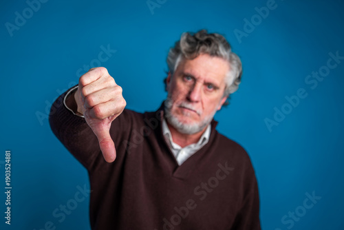 Canvas Print Mature man presenting a thumbs down gesture, expressing rejection, disappointmen