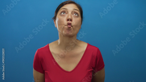 Slika na platnu Middle aged woman with dark hair tied back in red shirt purses lips and looks forward in studio; playfulness