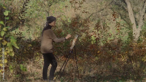 The artist paints a watercolor landscape of an autumn forest in sunny weather