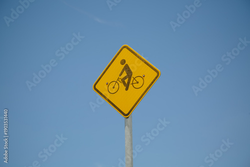 Placa de sinalização de trânsito alertando sobre ciclistas em treinamento, destacando segurança viária e conscientização no tráfego urbano e rural.