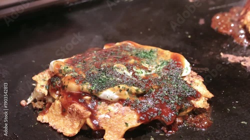 Okonomiyaki on a sizzling hot pan. Okonomiyaki is a savory Japanese pancake made from a flour batter mixed with cabbage, egg, and other fillings like meat or seafood