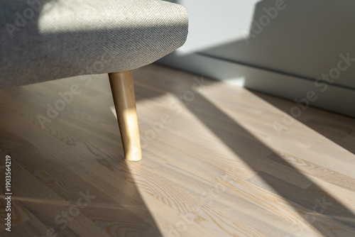 Bright sunlight shadows on wood floor by a modern grey bed