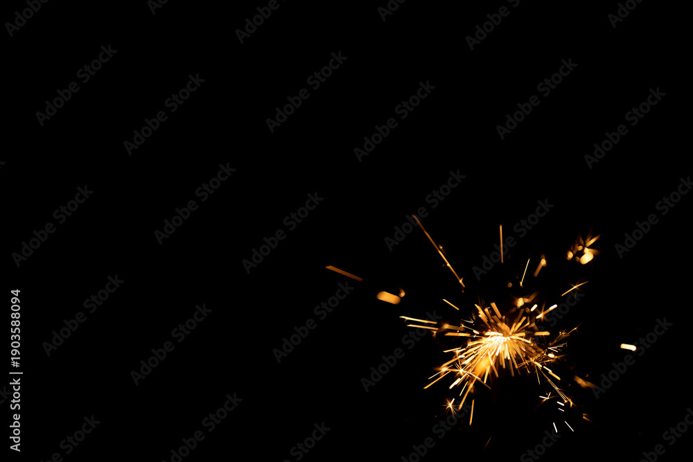 Fototapeta premium Sparkler emitting bright sparks against a dark background, showcasing individual sparks radiating outward in various directions, creating a dynamic visual effect