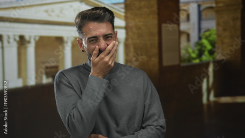 Tableau sur toile Man places hand on chest while laughing in front of an old university building facade under natural daylight; joy sincerity