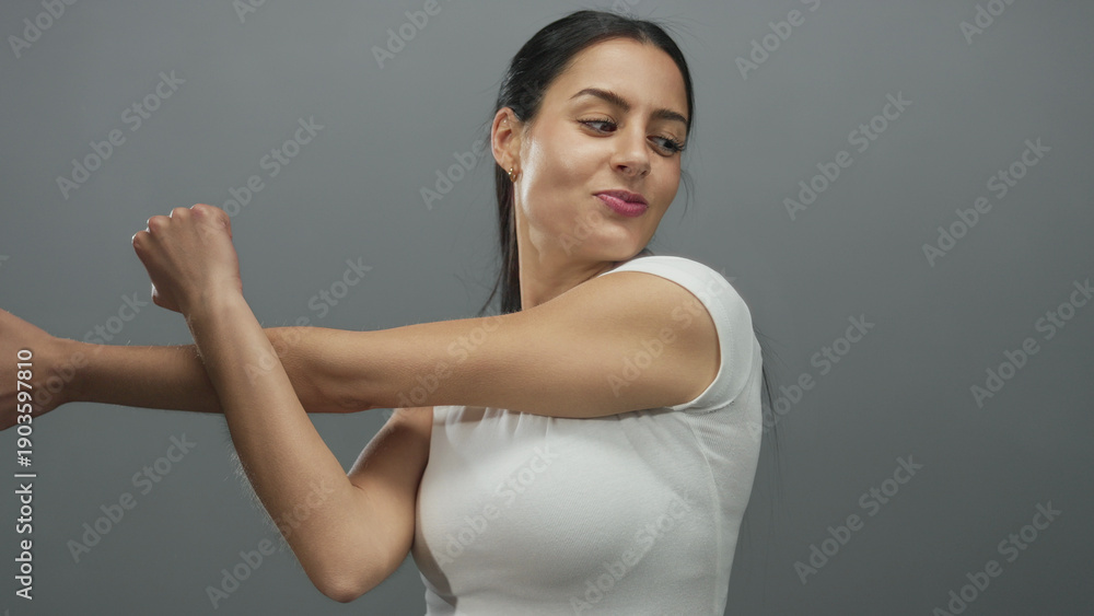 Obraz premium Young woman stretching against grey wall showcasing happiness and energy in an isolated studio environment with focus on fitness and personal well-being.