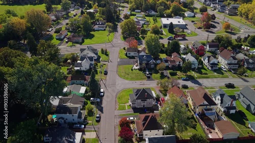 Aerial view of American suburban neighborhood with residential houses, intersecting streets, green yards, and autumn trees, showing low density housing, local infrastructure