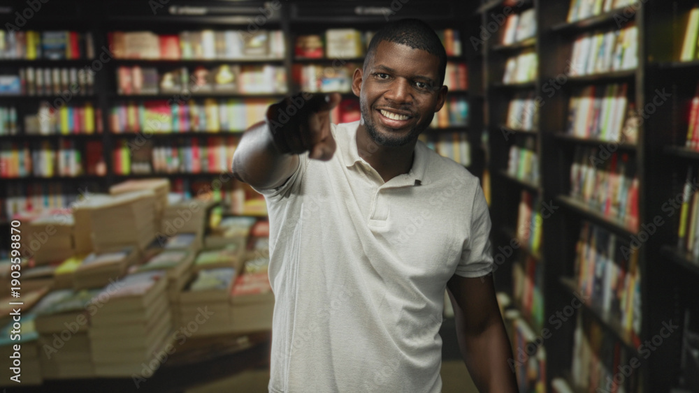 Fototapeta premium Man points finger toward camera in a busy bookstore building surrounded by bookshelves and stacked books wearing white polo; friendly confidence.