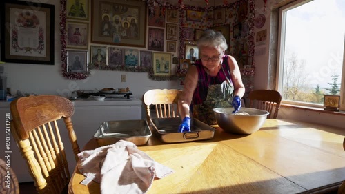 Elderly woman preparing dough balls for baking in a room full of religious orthodox icons in alaska