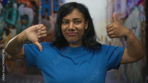 Tableau sur toile Woman gives thumbs up with right hand and thumbs down with left hand on street graffiti wall; choice indecision