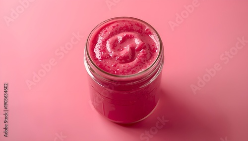 A vibrant pink smoothie in a glass jar against a pink background