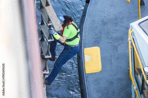 Foto Female ship pilot descending a rope ladder from a large commercial vessel to a p