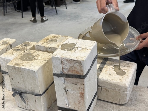 Demonstrates both casting and throwing techniques in the production of ceramic art . An artist pours liquid clay (slip) into plaster molds for ceramic pomegranate sculptures, wheel-turned clay pots.