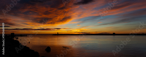 Fotografie Panoramic sunset with fiery orange sky over a calm sea and distant silhouettes