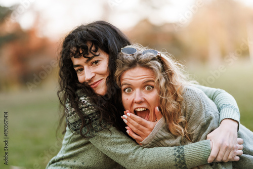 Fotografia Two friends embrace joyfully in a sunlit park while enjoying a delightful aftern