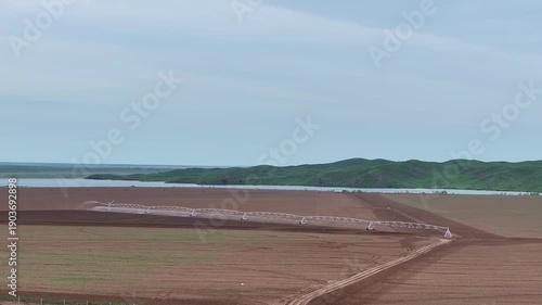 A wide cinematic view of a center-pivot irrigation system evenly watering agricultural land. The shot highlights the scale of the fields, the efficiency of modern agricultural technologies.