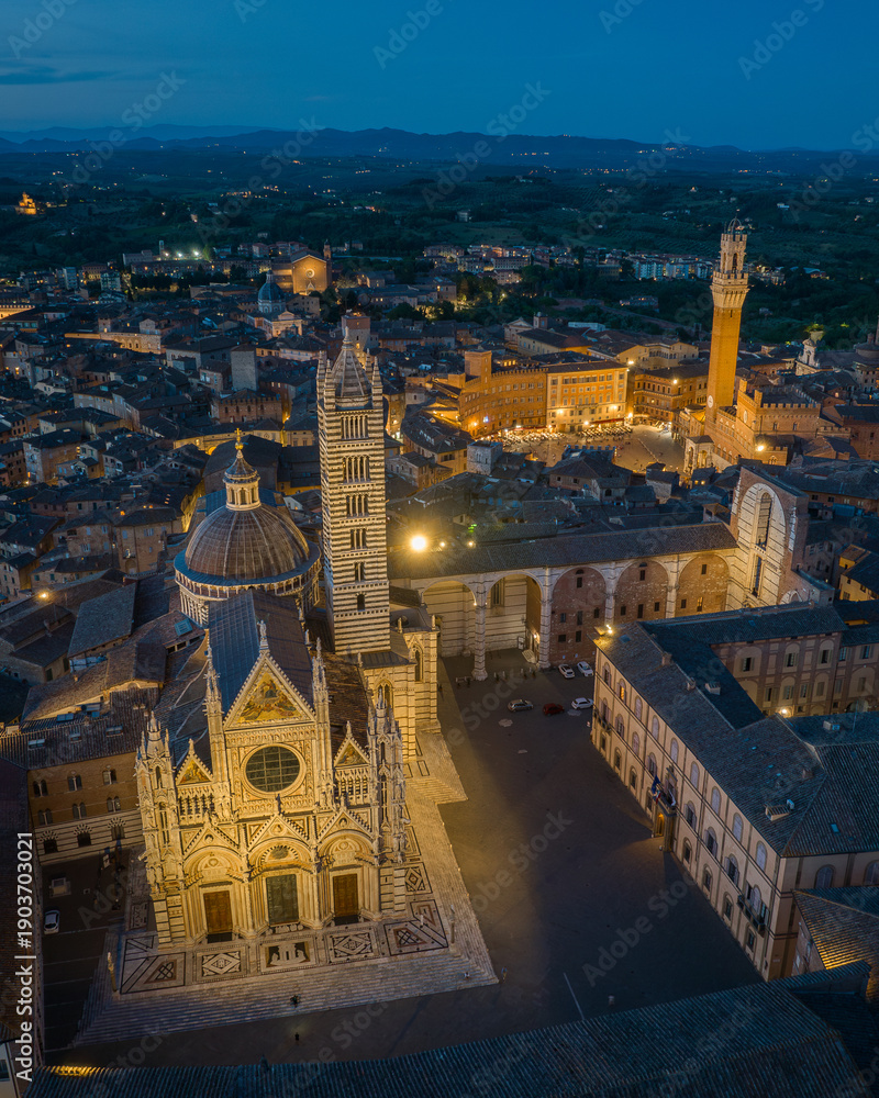 Fototapeta premium Aerial view of Siena Cathedral (Duomo di Siena) illuminated at blue hour, showcasing Gothic architecture and historic landmarks in the medieval city of Siena, Tuscany, Italy