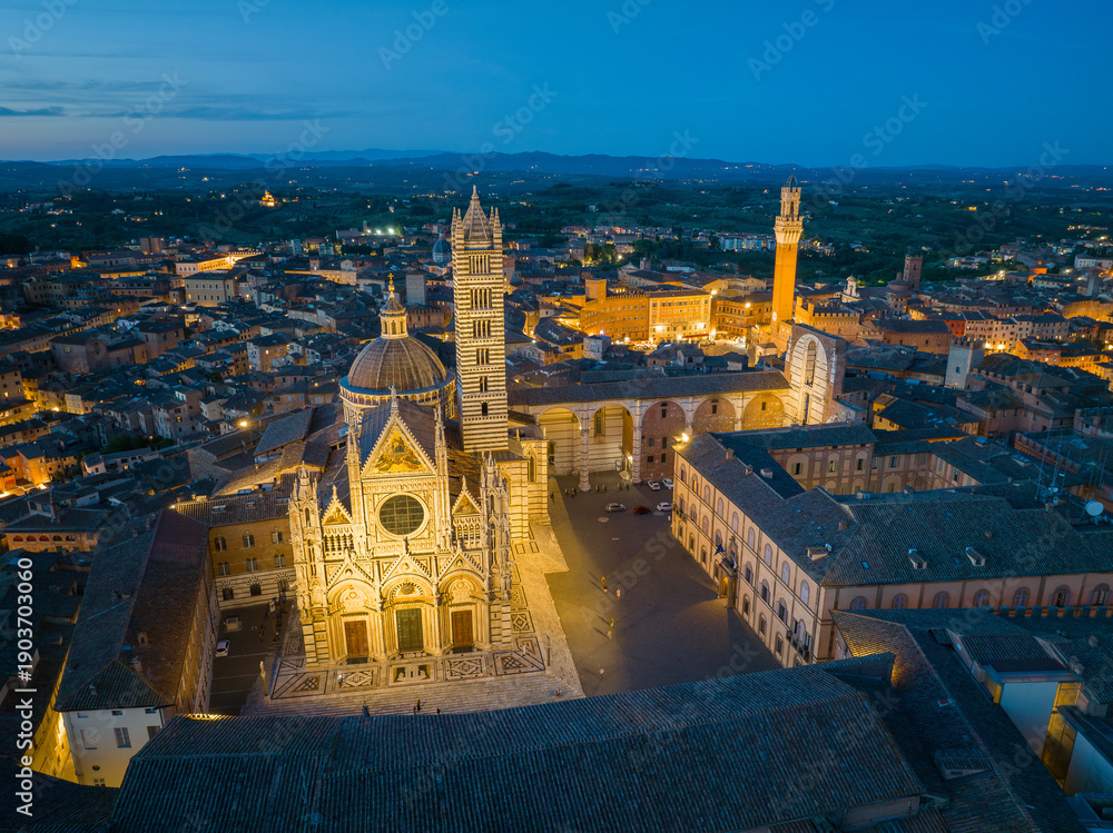 Fototapeta premium Wide panoramic aerial view of Siena at dusk, revealing the medieval old town, red rooftops, and surrounding Tuscan landscape. Classic Italian cityscape and UNESCO World Heritage Site